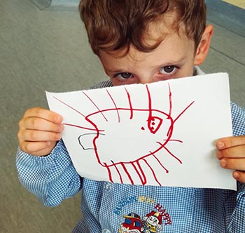 Bambino con il grembiulino dell'asilo che mostra un disegno raffigurante un insetto che rappresenta il coronavirus