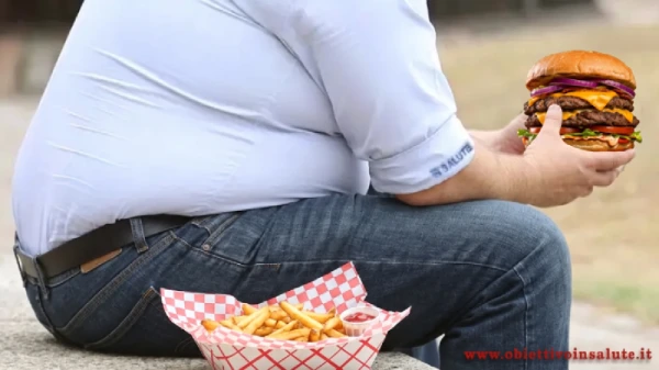Uomo obeso seduto nel parco con in mano un hamburger