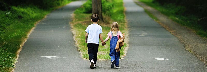 due bambini presi per mano che camminano verso il bivio