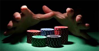 Due mani, che emergono dall'oscurità, afferrano delle fiches da poker accatastate sul tavolo verde da gioco