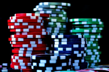 Immagine in cui delle fiches da poker sono accatastate sul tavolo verde da gioco in un fondo buio