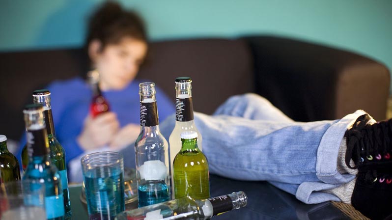 Ragazza ubriaca sul divano con le gambe sul tavolo pieno di bottiglie di liquore