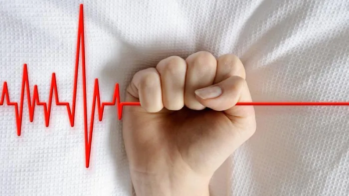 Una mano su un lettino stringe forte una linea di elettrocardiogramma tanto da farla diventare piatta