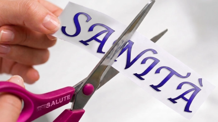 Una forbice taglia un foglio di carta con su scritto "Sanità"