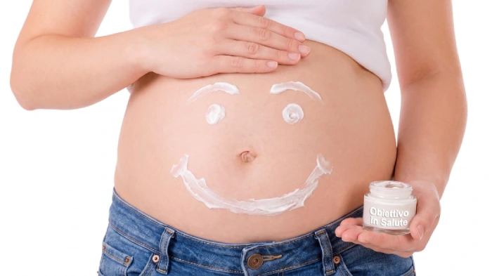 Donna in gravidanza che con la crema idratante disegna una faccia sorridente sul pancione